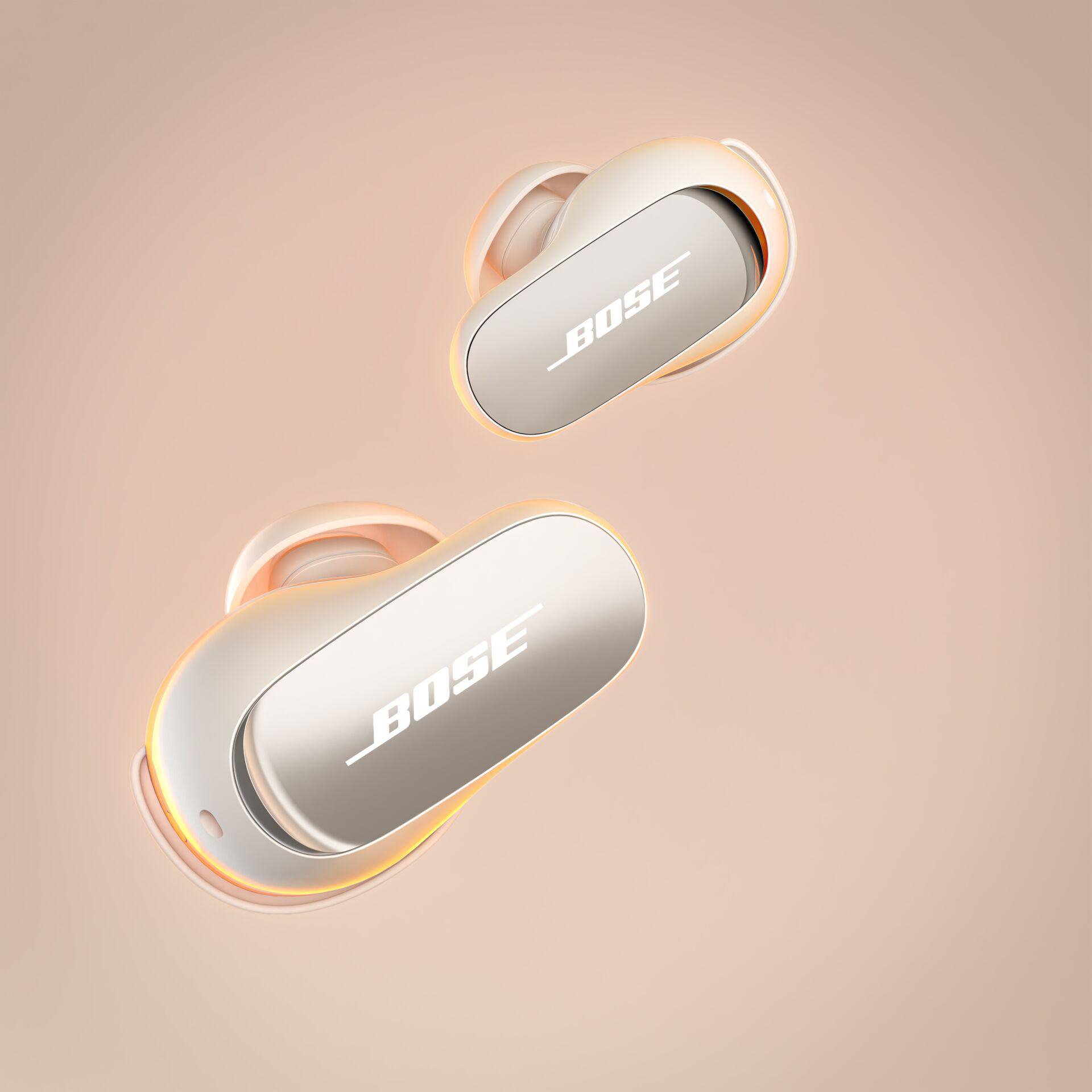 Zwei kabellose Bose-Ohrhörer auf hellpfirsichfarbenem Hintergrund mit Bose-Logo.