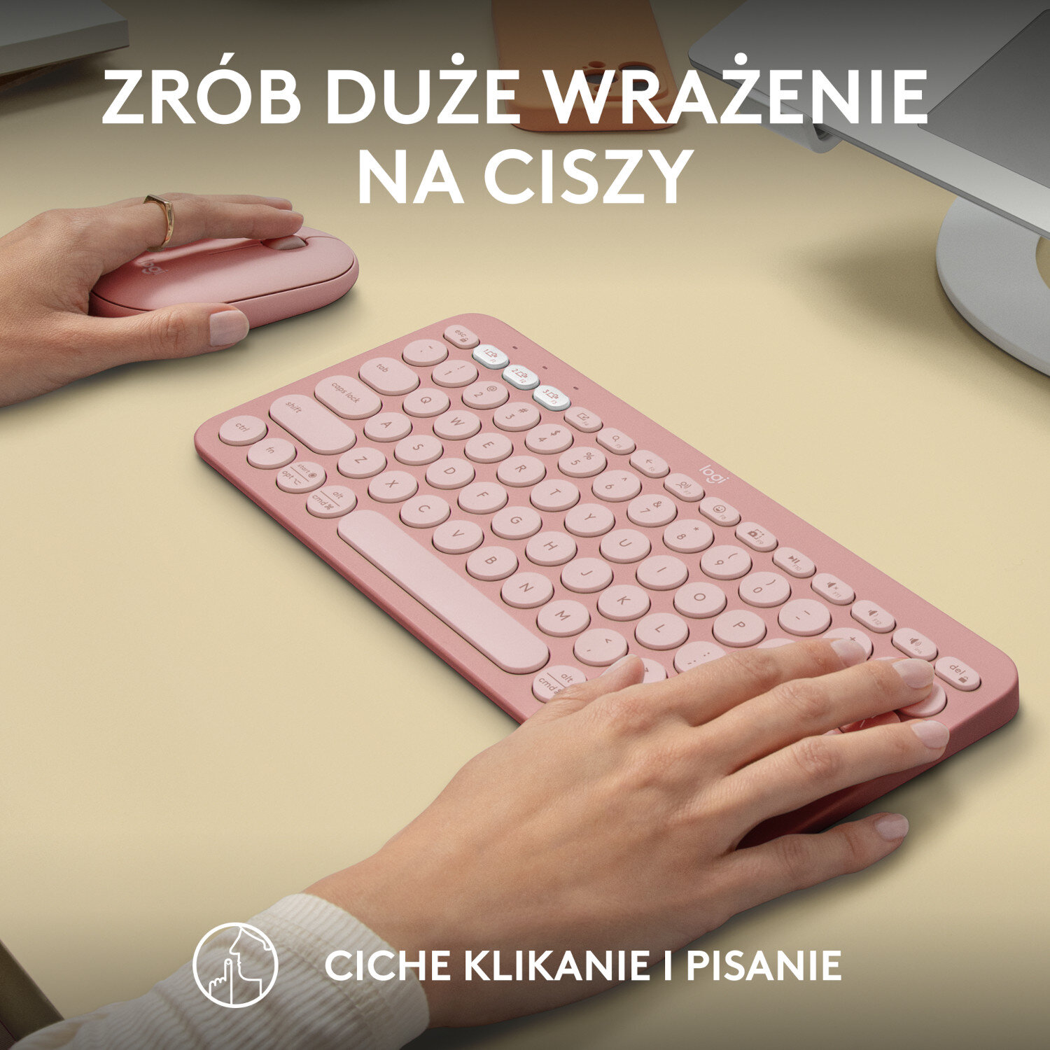 Różowy zestaw klawiatury i myszy na jasnobrązowej powierzchni, z rękami piszącymi.
