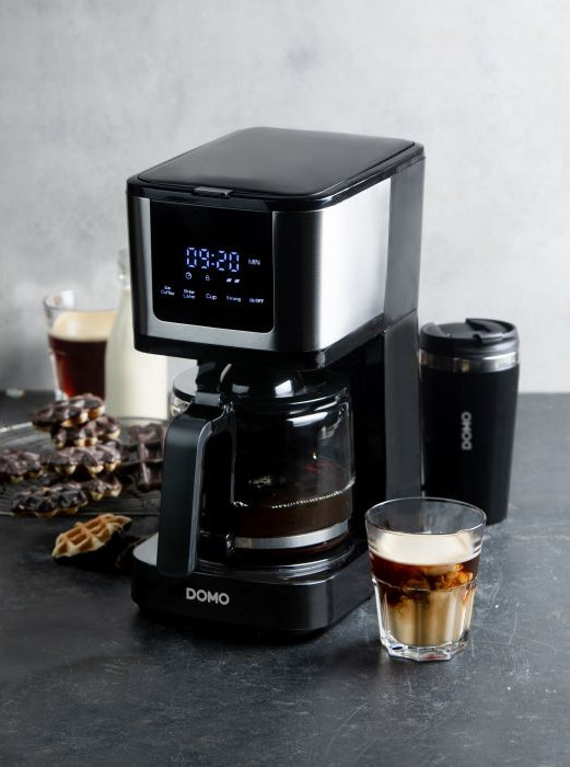 Zwarte koffiemachine met glazen kan en kopje, naast wafels.