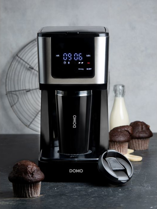 Koffiezetapparaat met een kopje en muffins op een donker oppervlak.