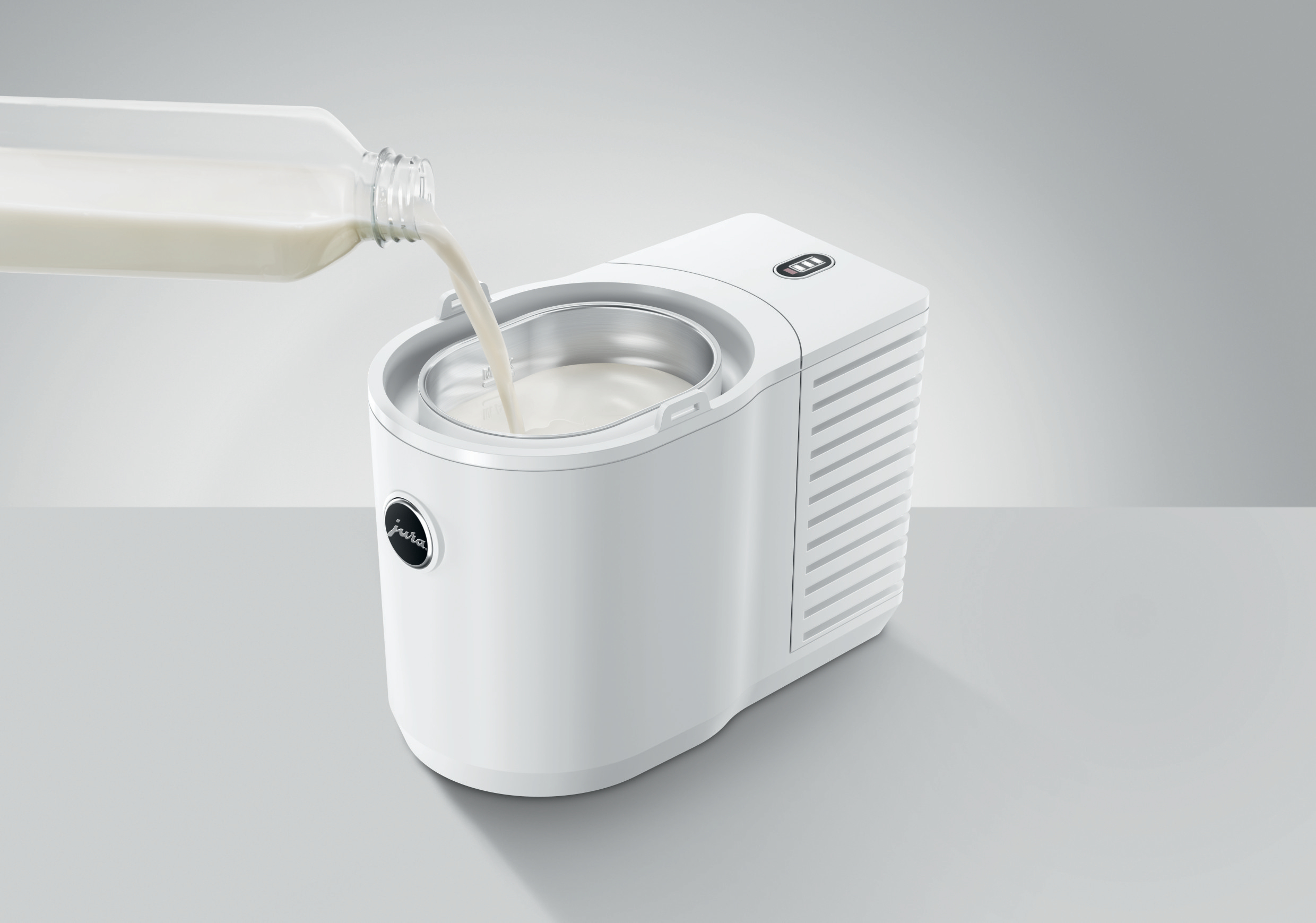 Weißer Eisbereiter mit Milch, die in die Schüssel gegossen wird.