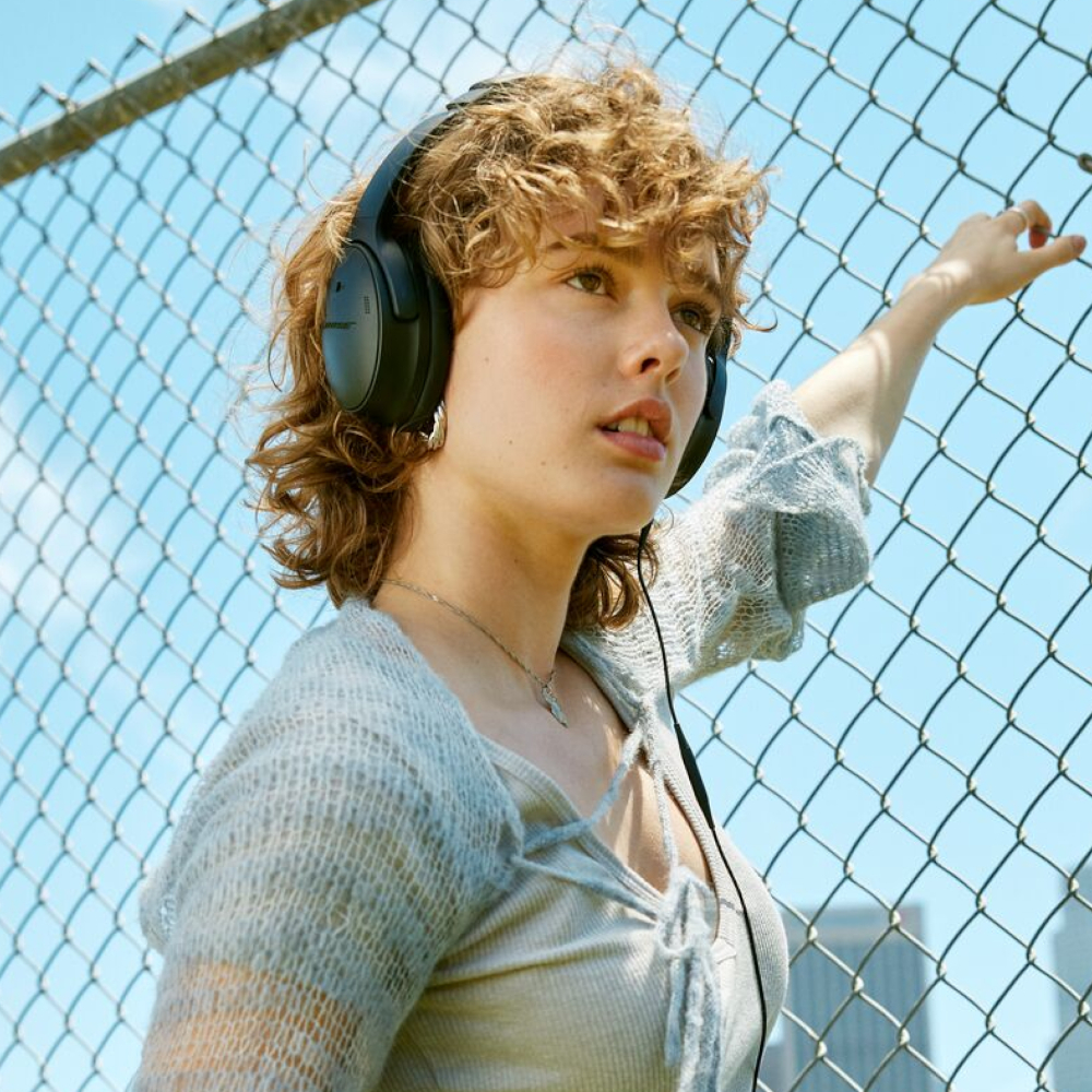 A woman wearing headphones near a fence.