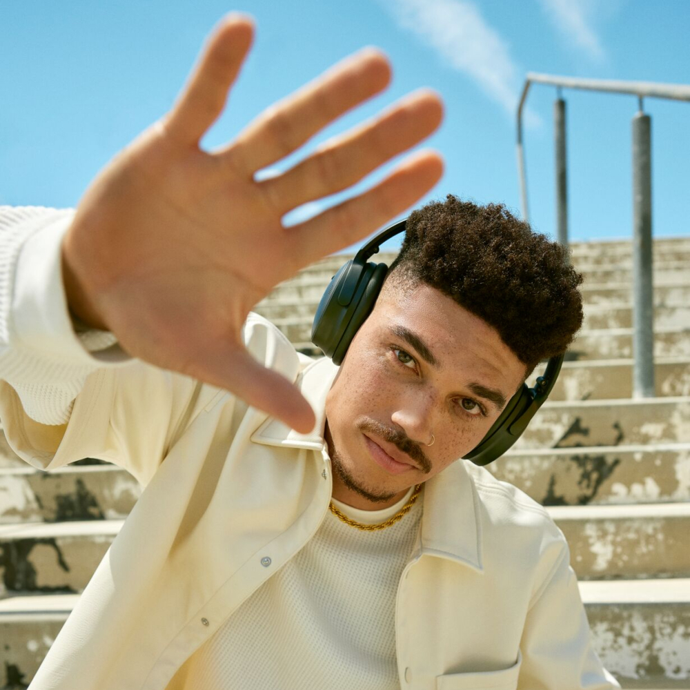 Man with headphones, hand up, looking at the camera.