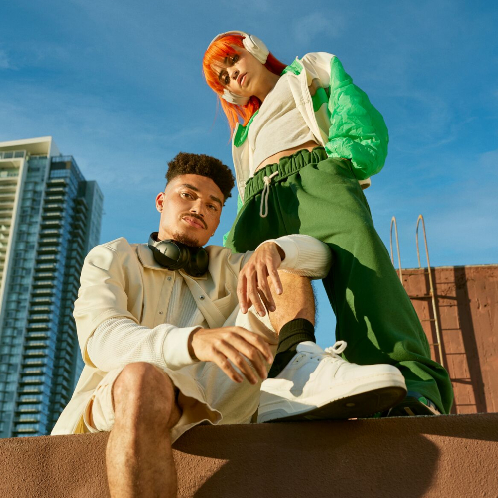 Two people on a rooftop, one wearing headphones, the other sitting and looking.
