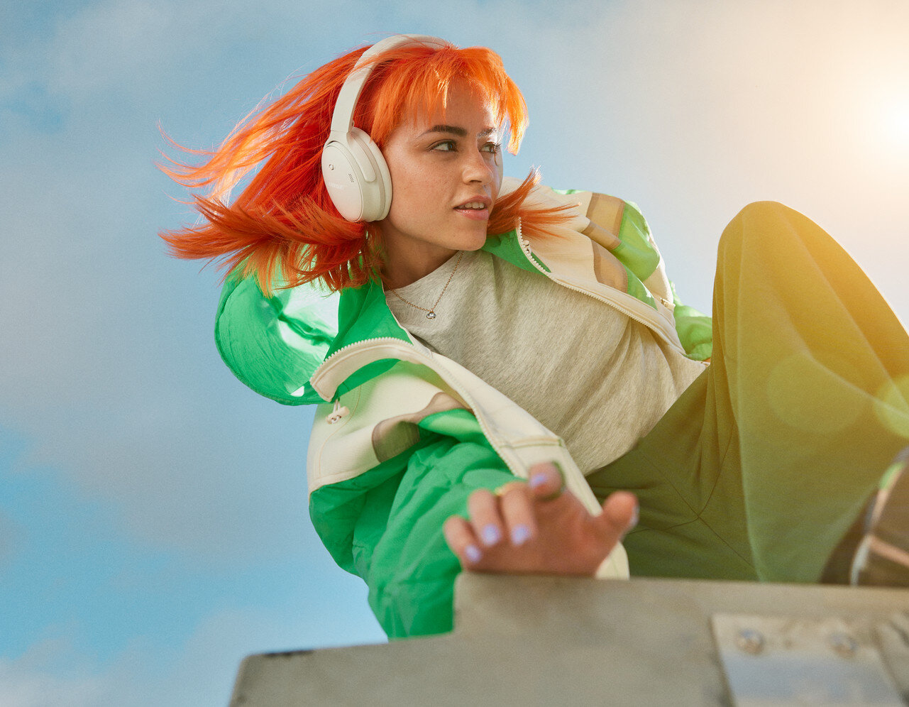 Kobieta z pomarańczowymi włosami i białymi słuchawkami uśmiecha się patrząc w bok.