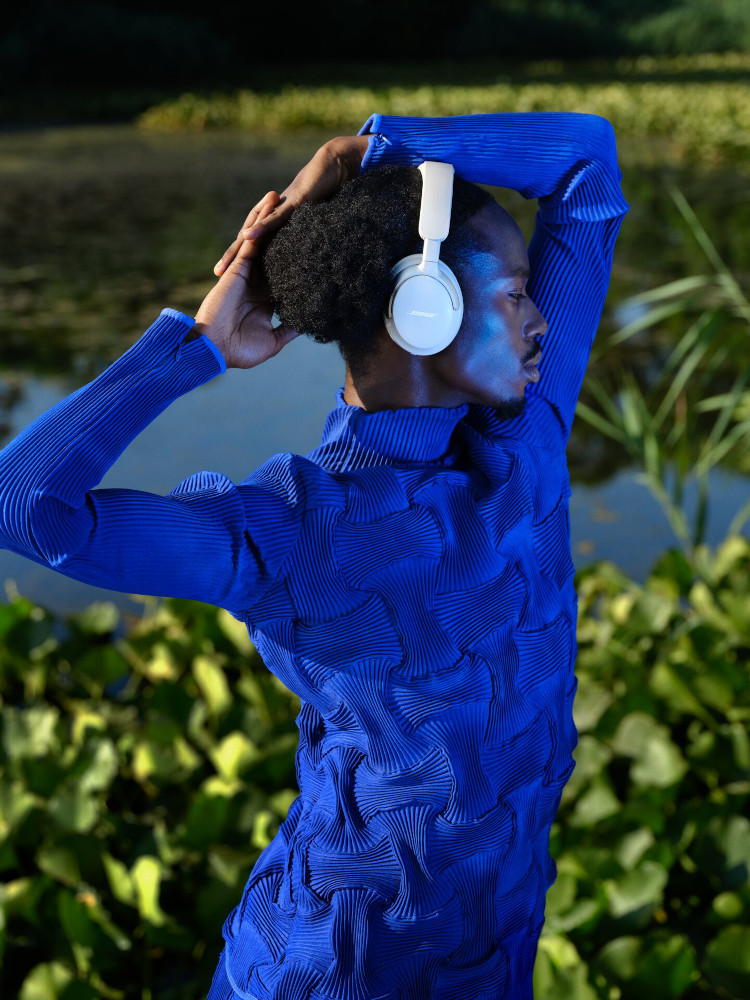Persoon met blauwe outfit en witte koptelefoon. Staat voor een meer met waterlelies.