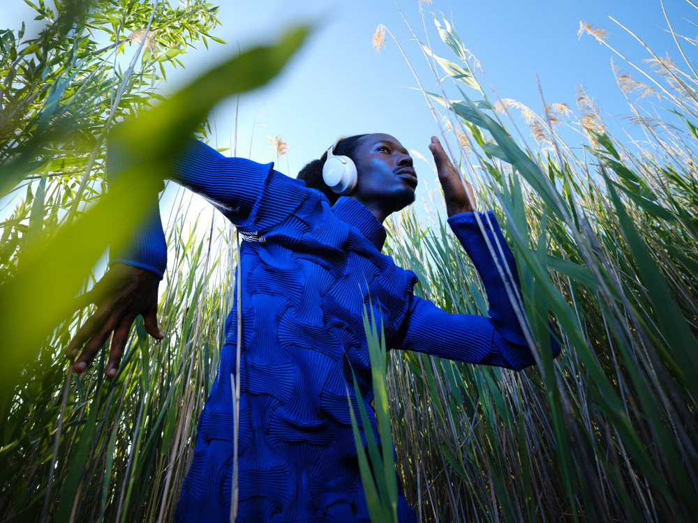 Een man in een blauwe outfit met een koptelefoon die door lang gras rent.