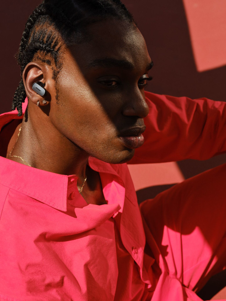 A dark-skinned man wearing a red shirt and gray earbuds. He is looking away from the camera.
