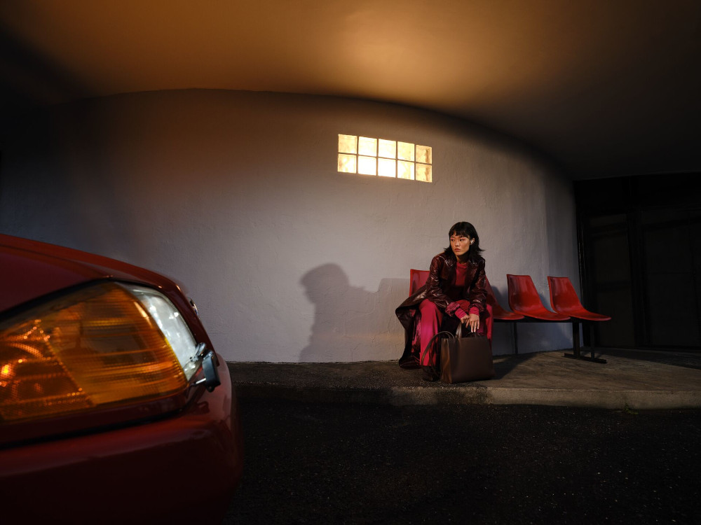 Een vrouw in rode kleding zit 's nachts bij een auto, onder een verlichte constructie.