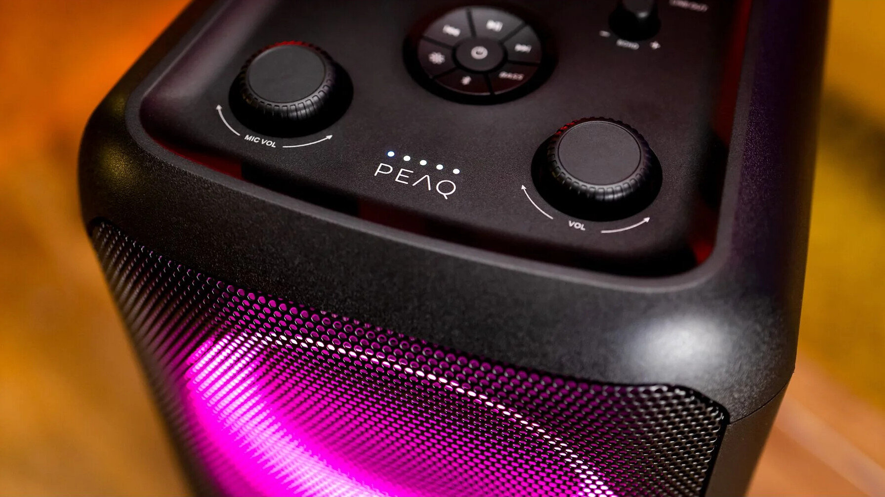 Czarny głośnik z różowymi i fioletowymi światłami, z pokrętłami na górze.