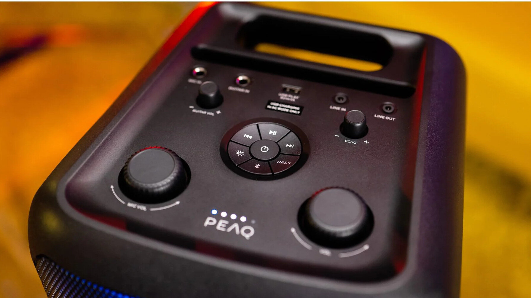 Czarny głośnik PEAQ z przyciskami, pokrętłami i uchwytem, z niebieskim oświetleniem na dole.