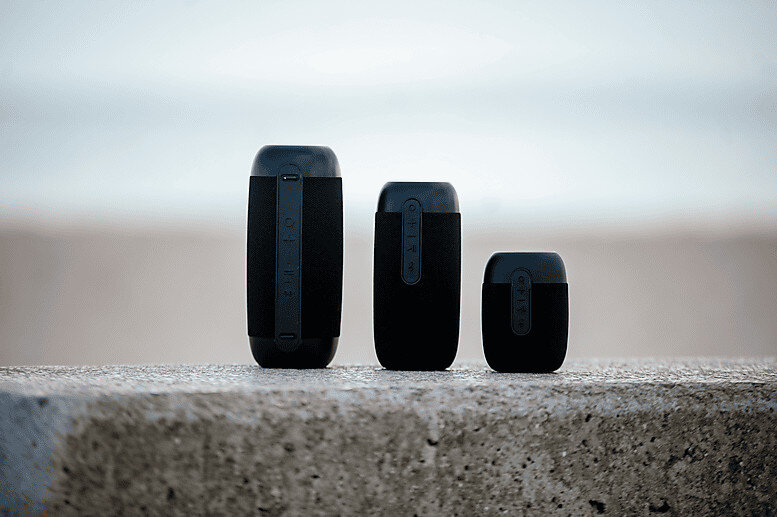 Trzy czarne głośniki o różnych rozmiarach na betonowej powierzchni.