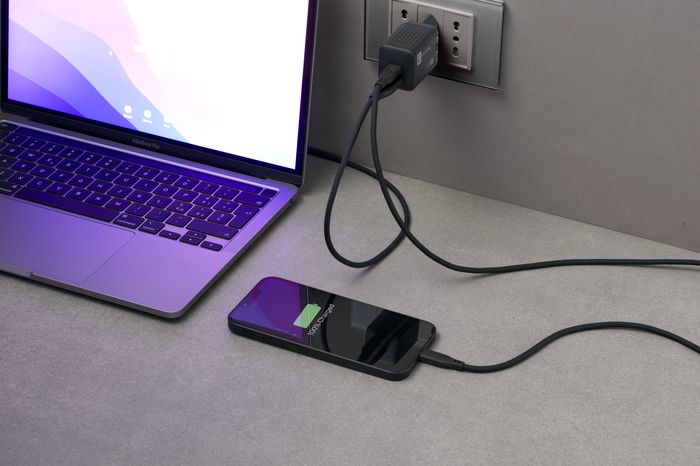 Laptop lädt mit einem Telefon. Beide sind über schwarze Kabel an einer Steckdose angeschlossen.