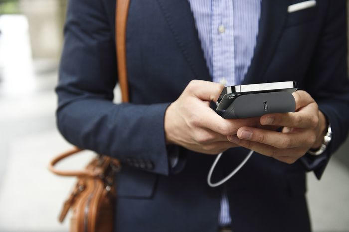 Mann im Anzug hält Telefon und Ladegerät, Tasche im Blick.