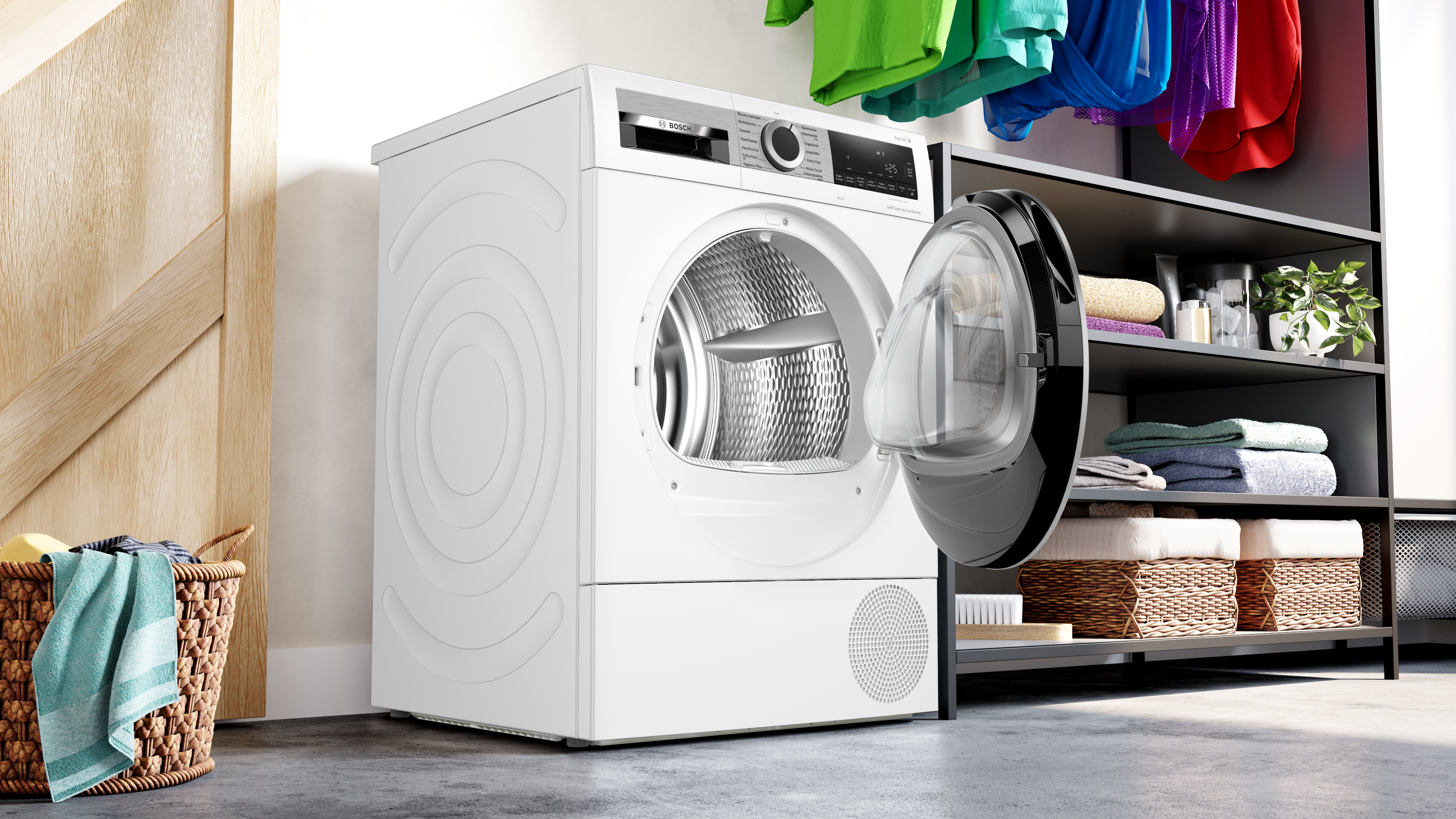 Weiße Waschmaschine mit offener Tür, neben einem Wäscheständer mit Kleidung. Weiße Wand und Holztür.