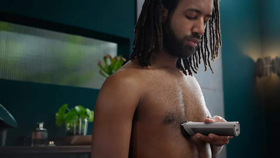 Mężczyzna goli klatkę piersiową trymerem w łazience.