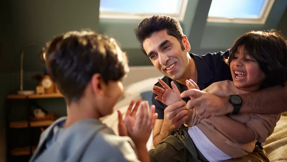 Uśmiechnięty ojciec bawiący się z dwójką dzieci na łóżku, w pokoju z oknami.