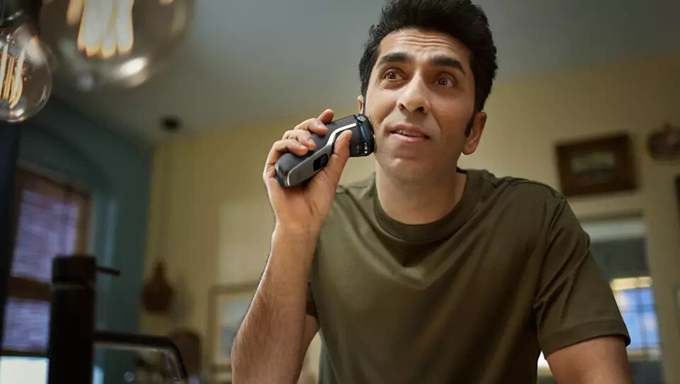 Mężczyzna goli twarz golarką elektryczną w łazience.