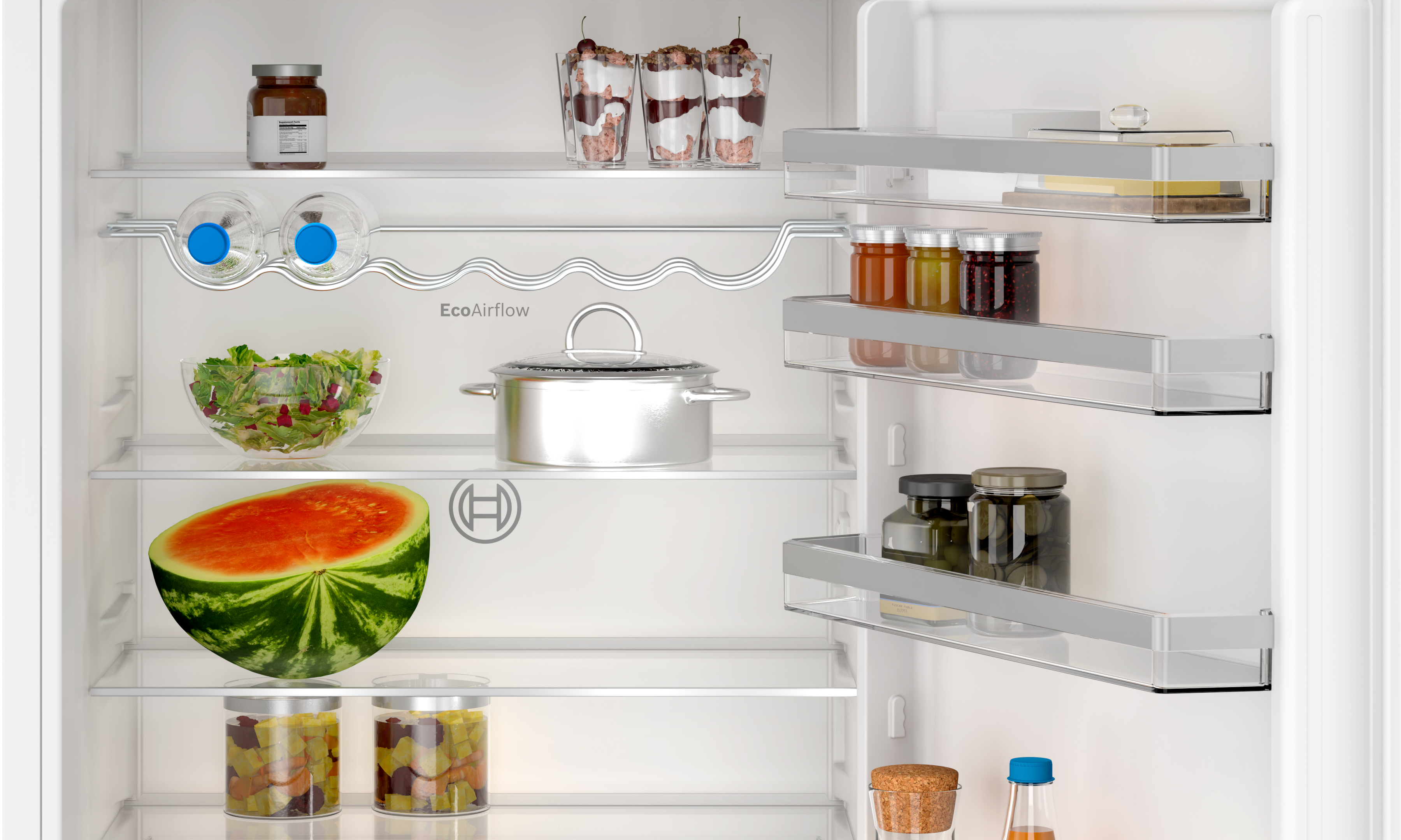 Ein Kühlschrankinnenraum, gefüllt mit Lebensmitteln. Enthält eine Wassermelone, Marmeladengläser, Salat und andere Artikel.