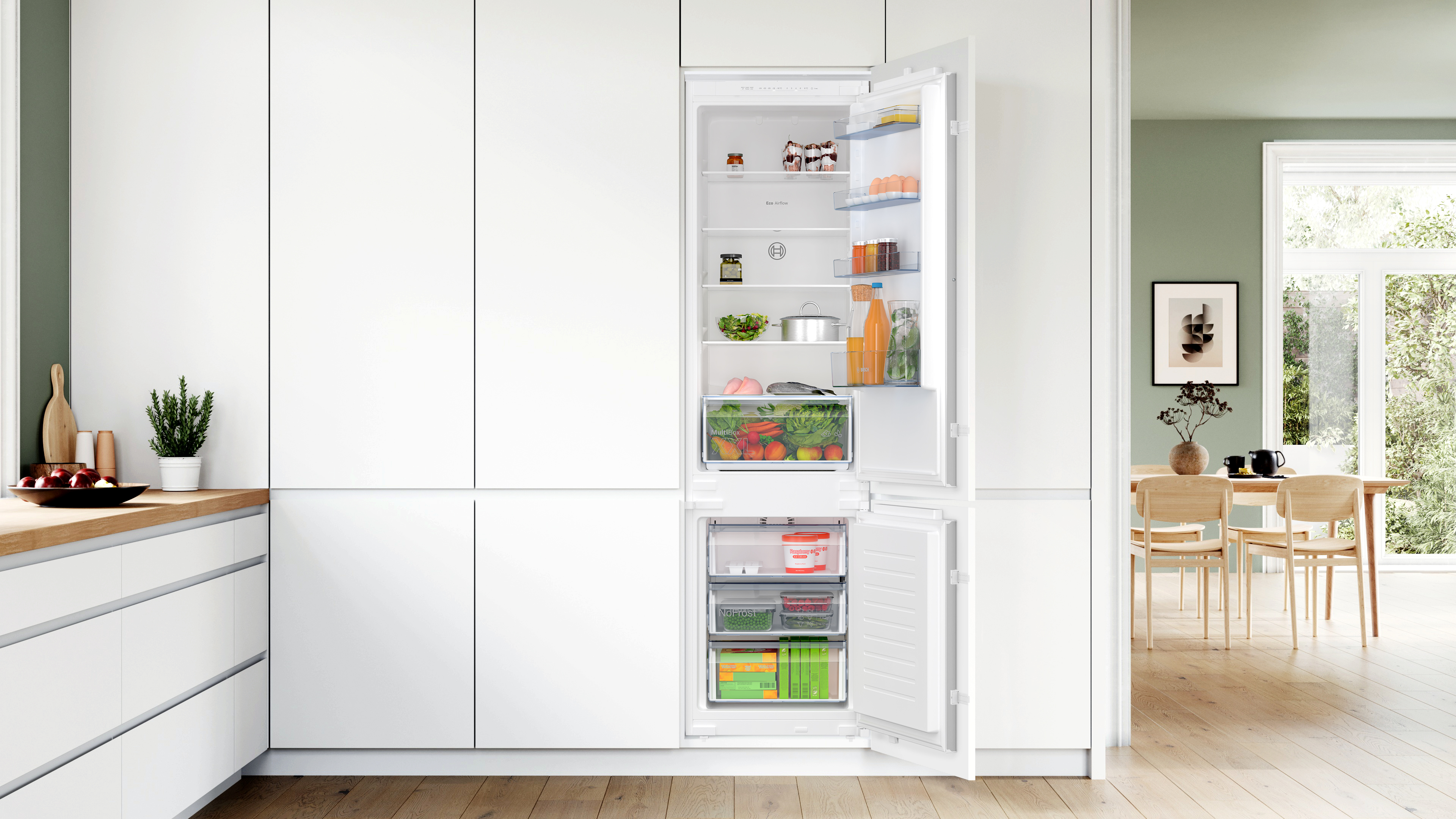 Ein offener, integrierter Kühlschrank mit Lebensmitteln, eingebaut in eine weiße Küche mit Essbereich.