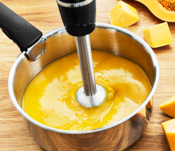 Kézi mixer egy sárga leveses fazékban, tökdarabokkal.