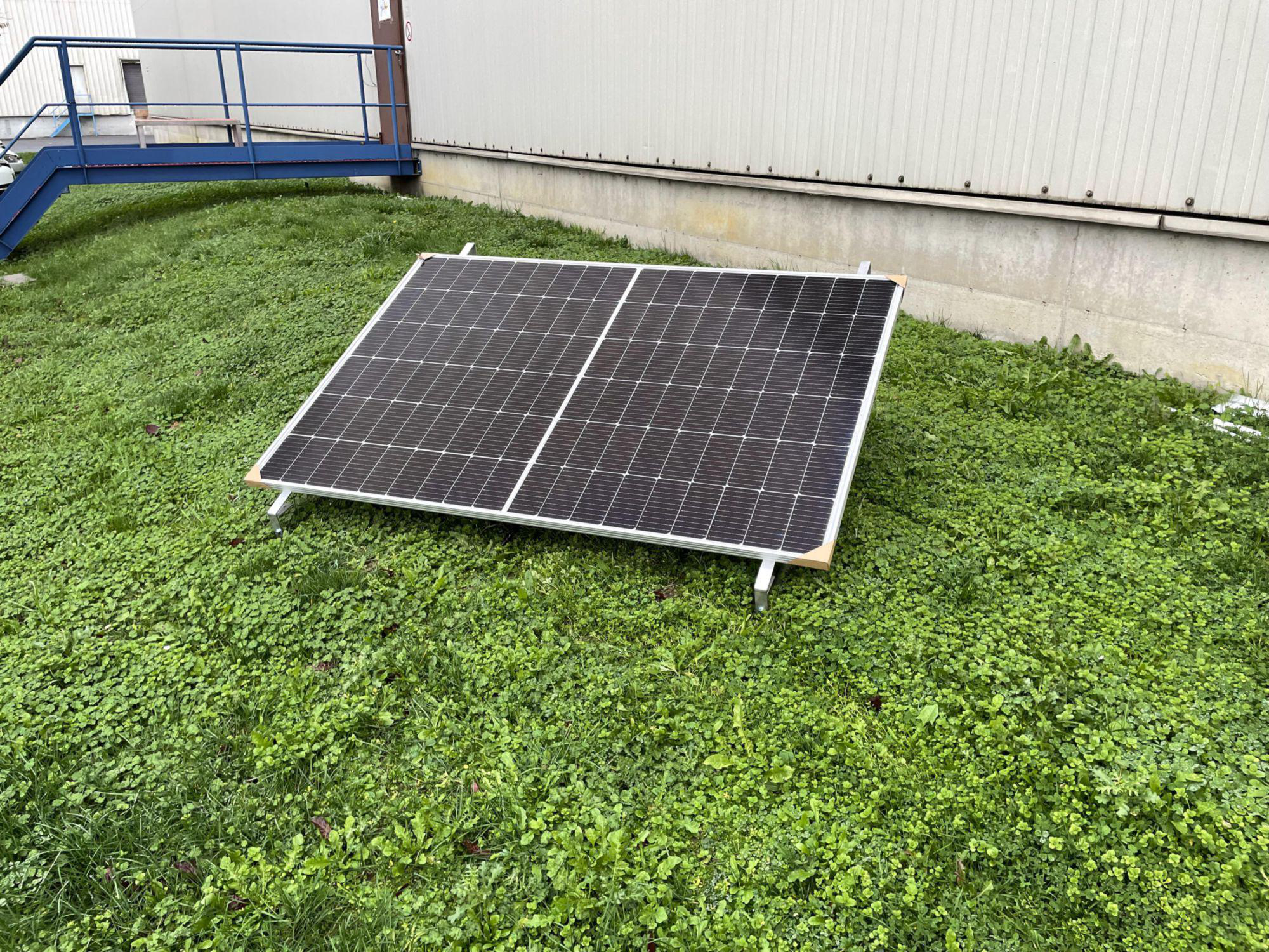 Solarpanel auf grünem Gras. Gebäude mit Treppe im Hintergrund. Bewölkter Himmel.