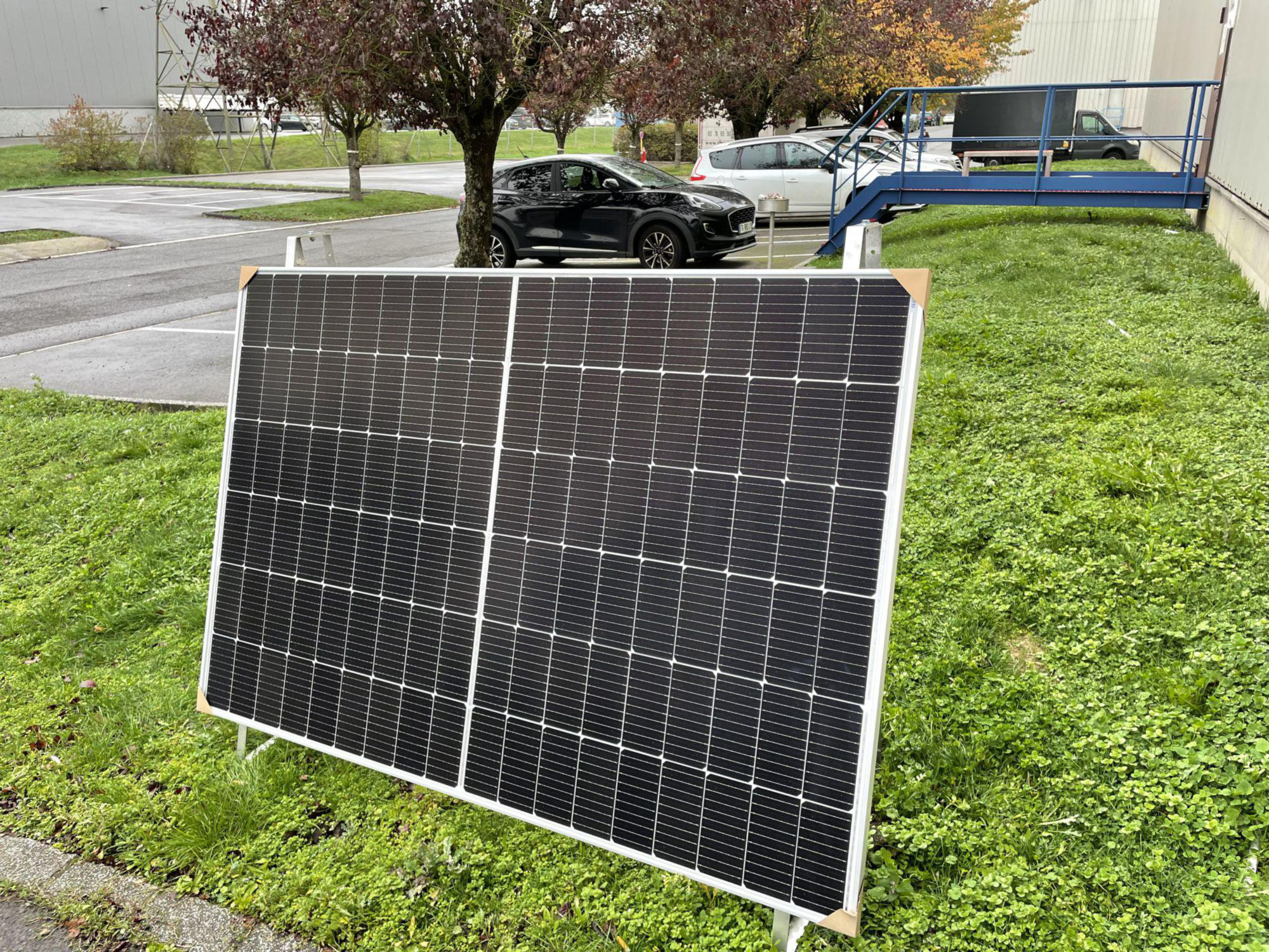 Große Solaranlage auf einer Rasenfläche, mit einem Auto im Hintergrund.