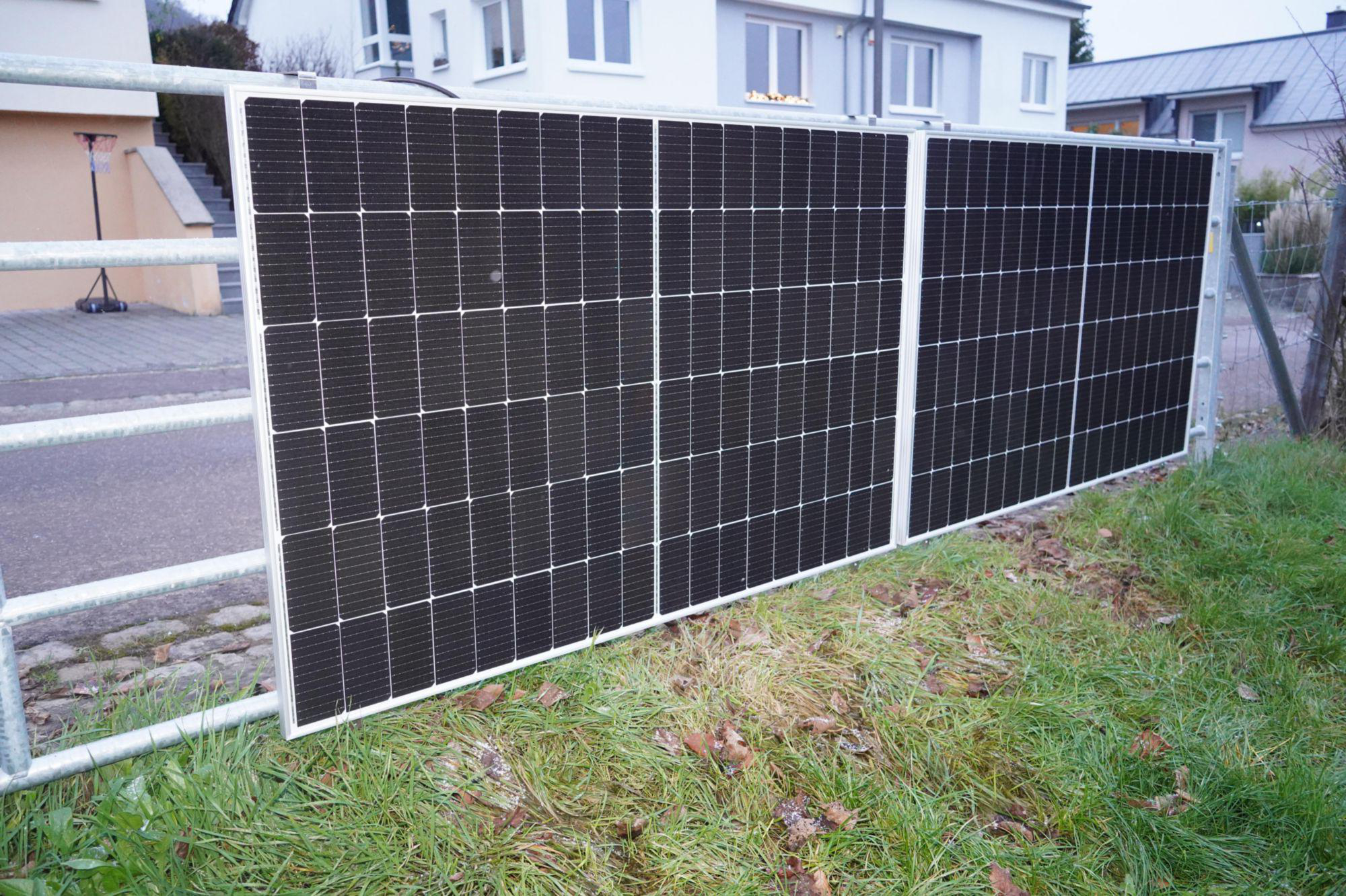 Solarpaneele an einem Tor, grünes Gras, Wohnhäuser im Hintergrund.