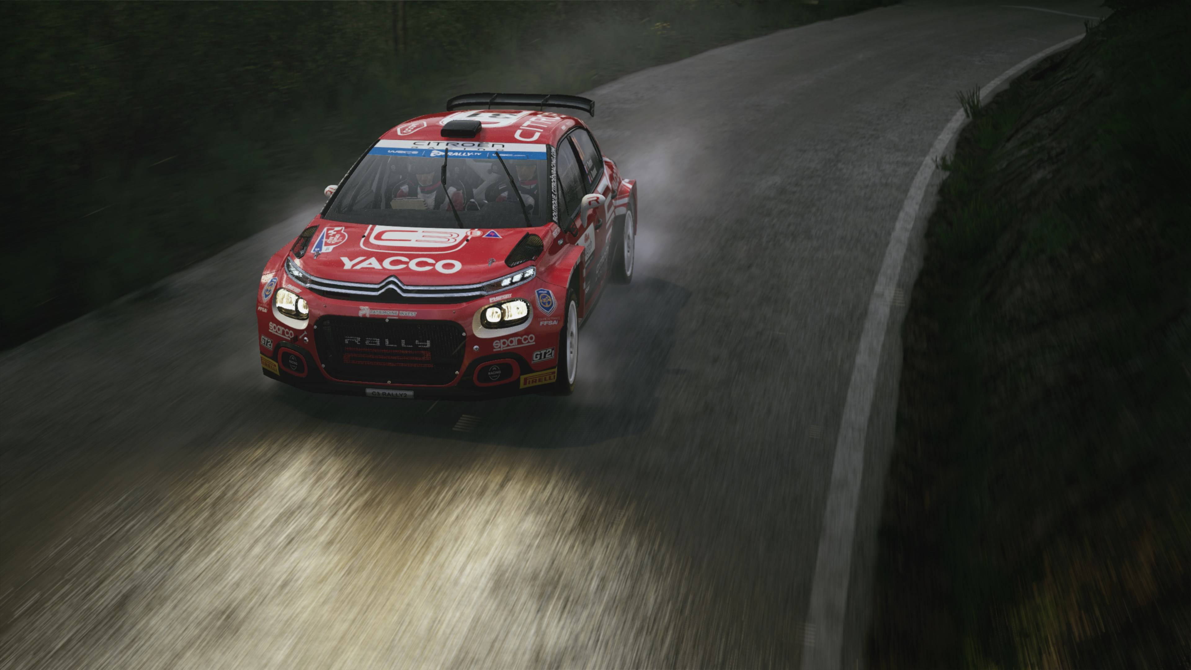 Une voiture de rallye Citroën rouge roulant à toute vitesse sur une route mouillée bordée d'arbres.