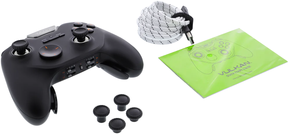 Fekete játékvezérlő fekete joystickokkal és extra joystick sapkákkal, egy zöld kézikönyv mellett.