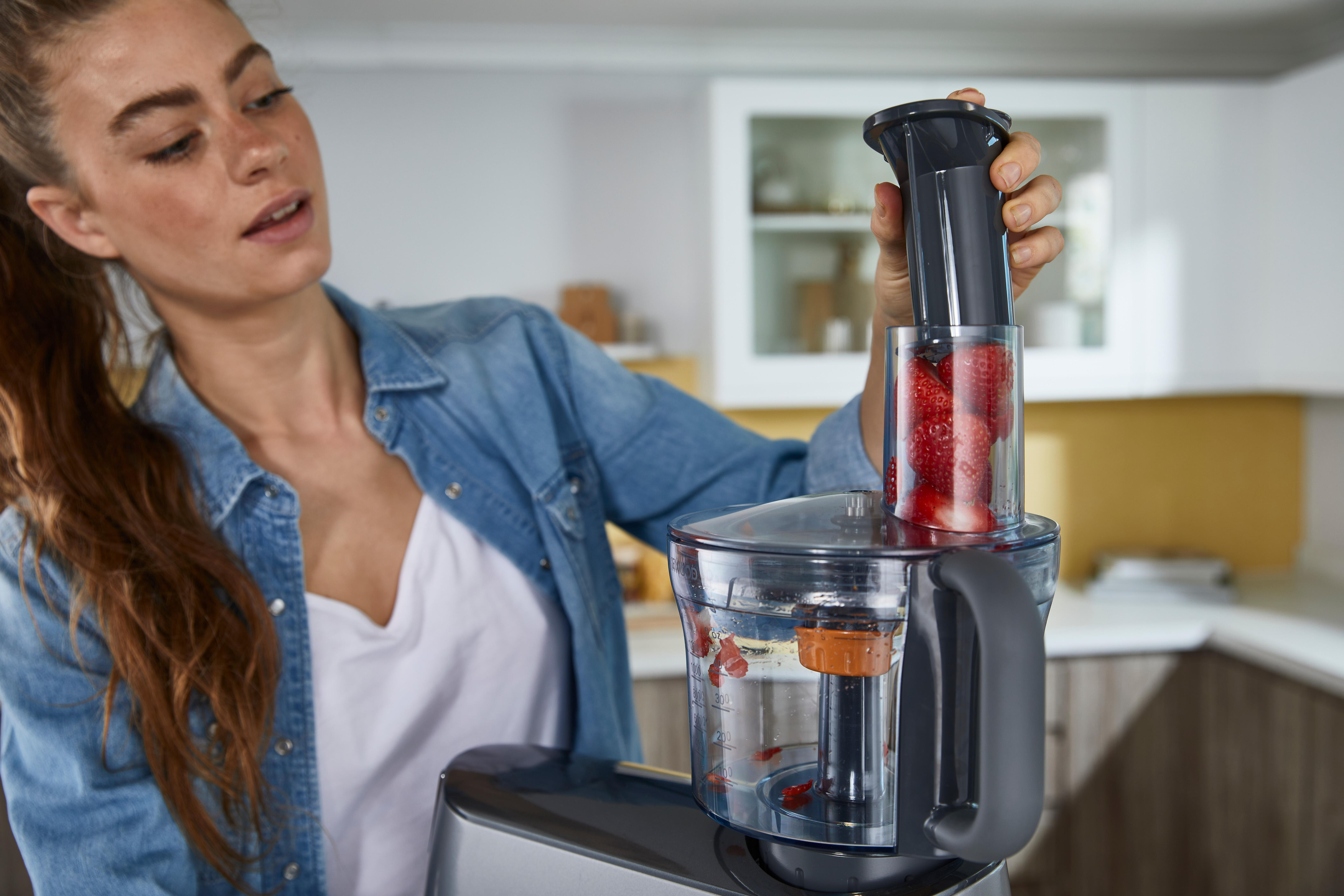 Frau gibt Erdbeeren in eine Küchenmaschine; Küche im Hintergrund.