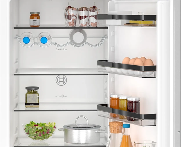 Nyitott hűtőszekrény ételekkel: üvegek, tojások, saláta és egy fazék. A polcok tárgyakat, EcoAirflow-t és accent line-t tartalmaznak.