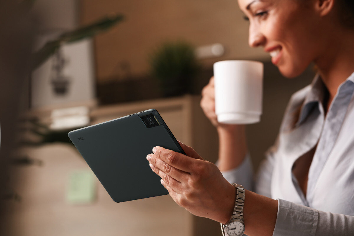 Kobieta trzyma tablet, uśmiechając się podczas picia z białego kubka z rozmytym tłem.