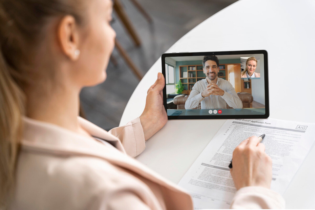 Kobieta podczas rozmowy wideo, trzymająca tablet z dwiema osobami na ekranie.