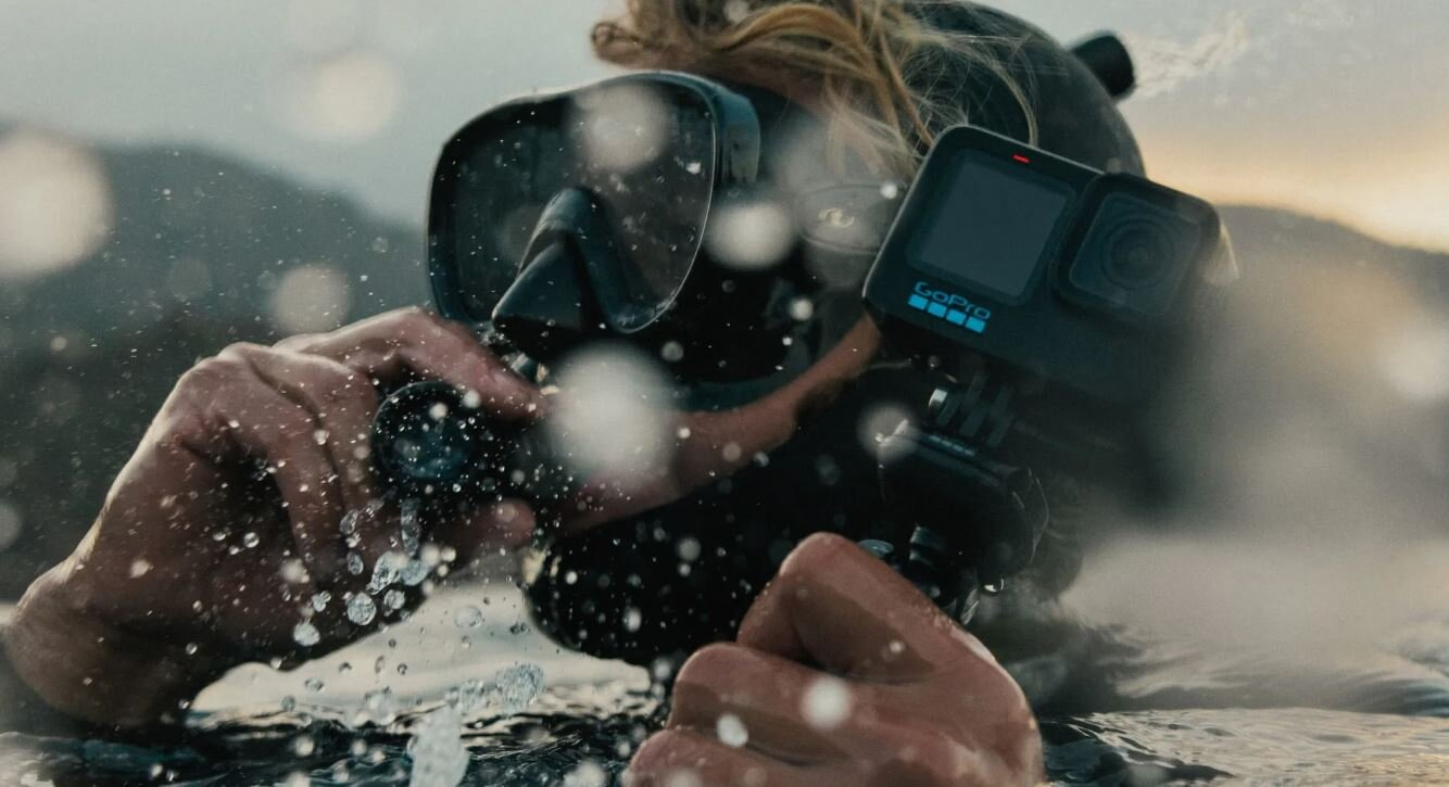Osoba w piankowym kombinezonie używająca kamery GoPro pod wodą, rejestrująca plusk wody.