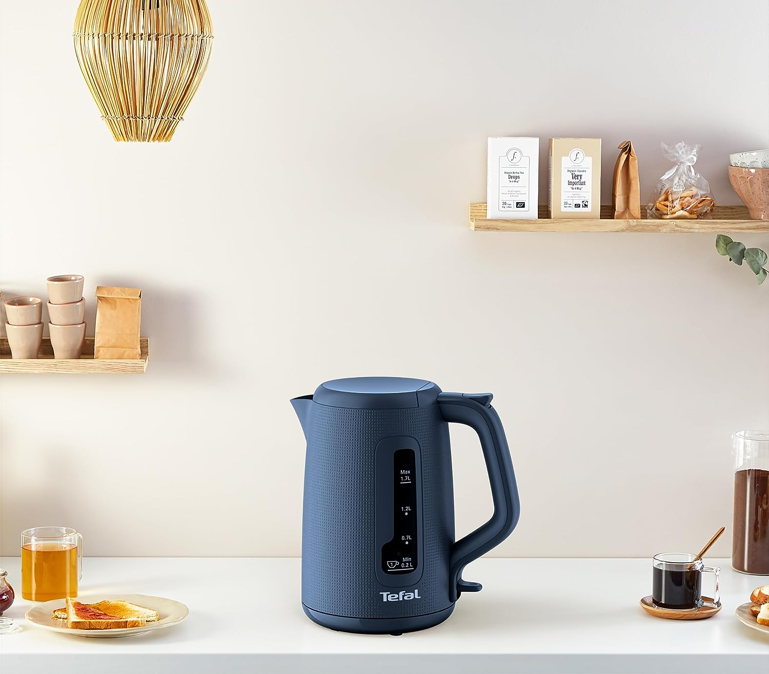 Blauer Wasserkocher auf weißer Arbeitsplatte, mit Toast und Marmelade, sowie einer Kaffeetasse.