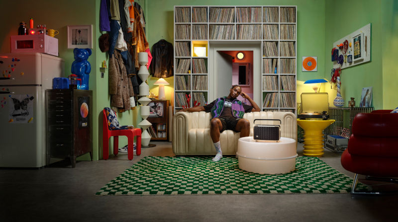 Ein Mann sitzt auf einer Couch in einem Raum mit Schallplatten, einer Stereoanlage und anderer Vintage-Dekoration.