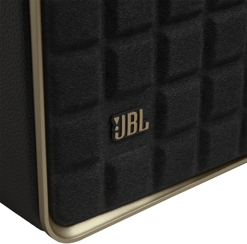 Nahaufnahme eines schwarzen Lautsprechers mit goldenem Rahmen und JBL-Logo. Der Lautsprecher hat eine Steppstruktur.