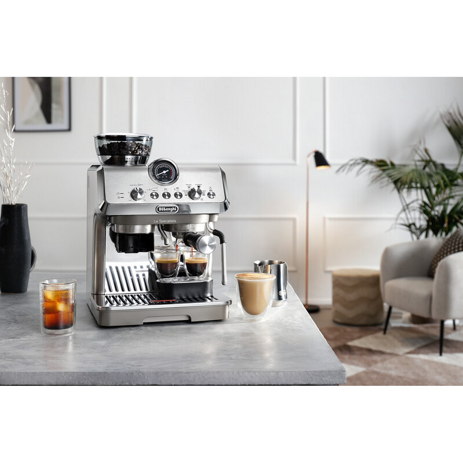 Een roestvrijstalen espressomachine met twee espressokopjes en een glas ijskoffie.