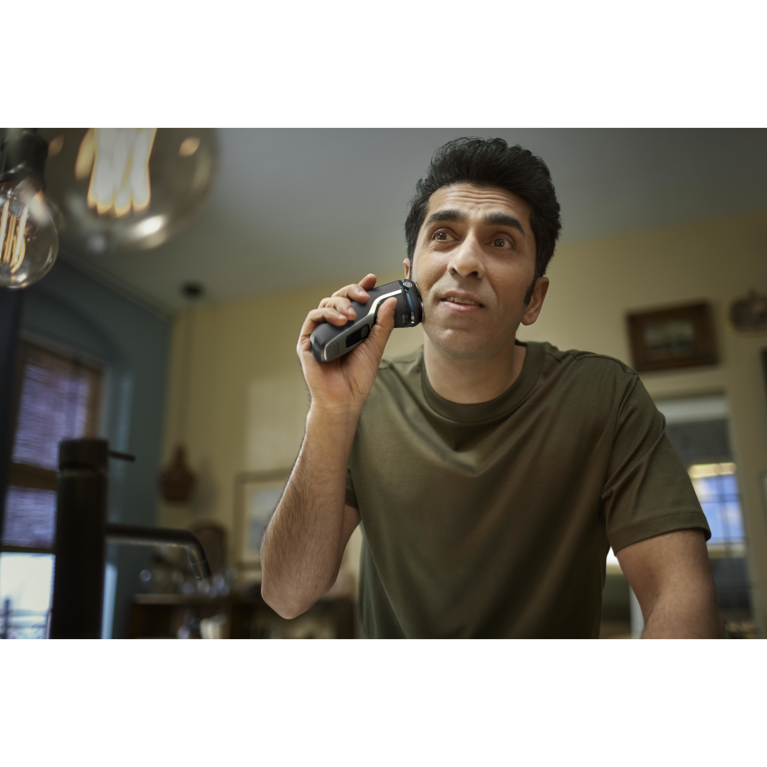 A man shaves his face with an electric razor, looking up.