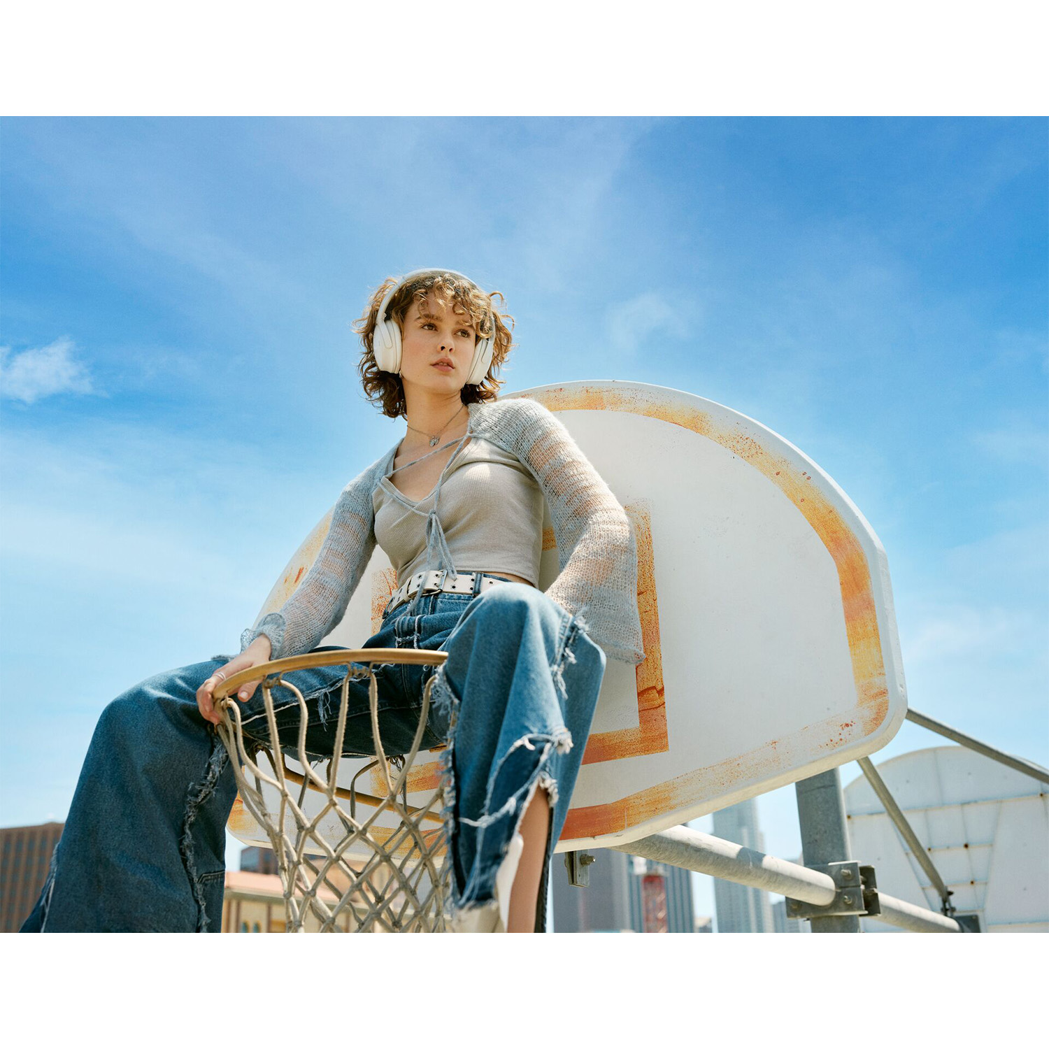 Una giovane donna è seduta su un canestro da basket con le cuffie sotto un cielo blu.