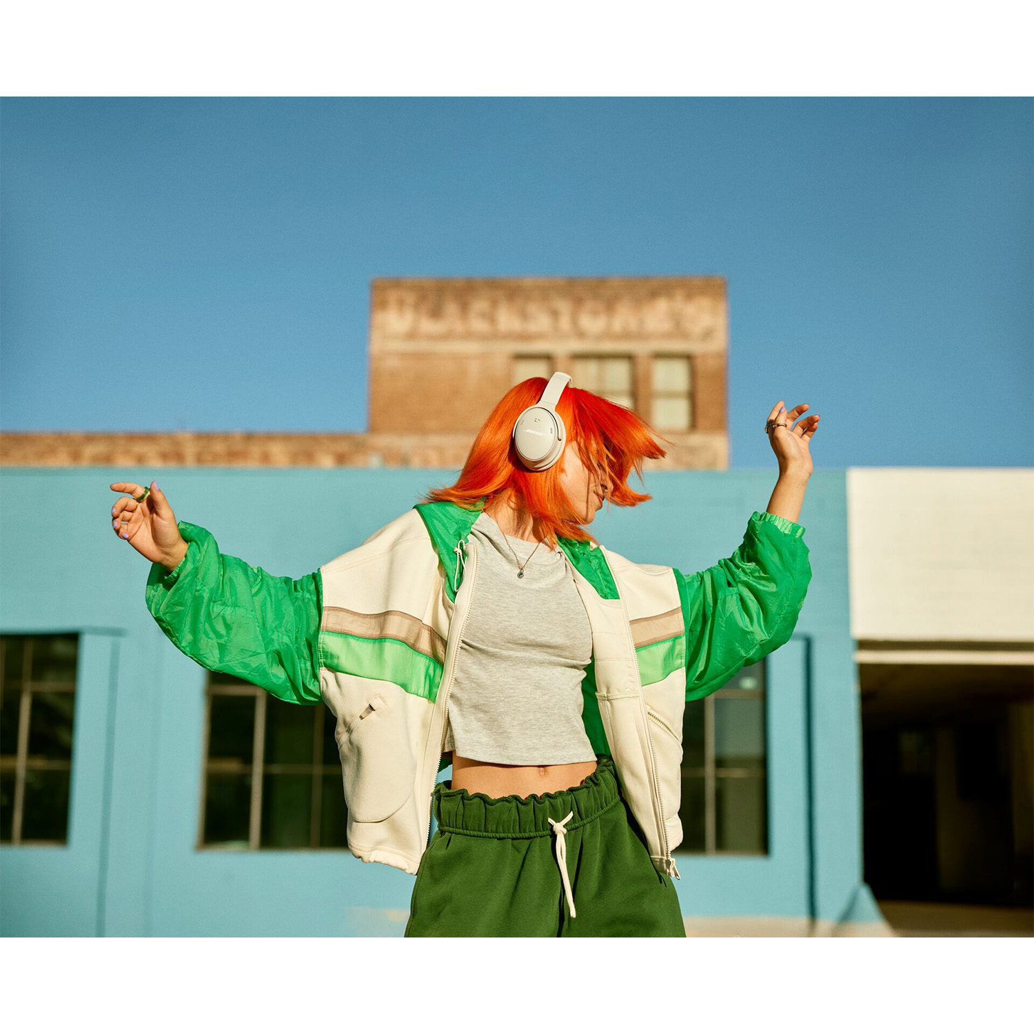 Donna con capelli arancioni che balla all'aperto, indossa le cuffie e una giacca verde.