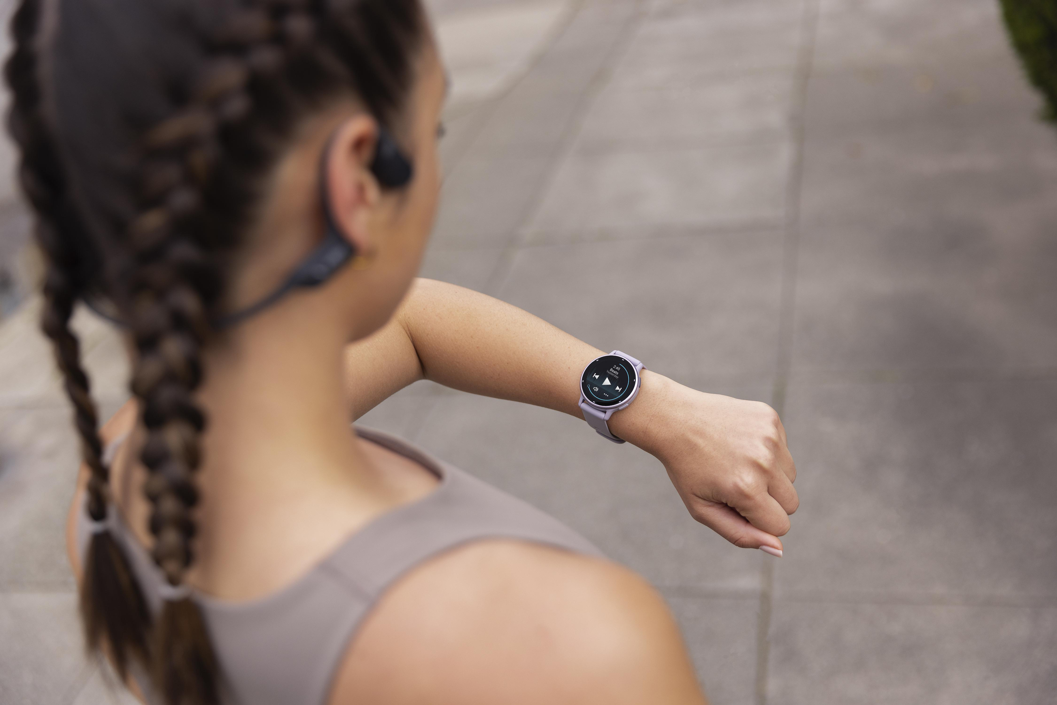 Frau mit Uhr am Handgelenk, blickt nach unten. Sie trägt Kopfhörer.