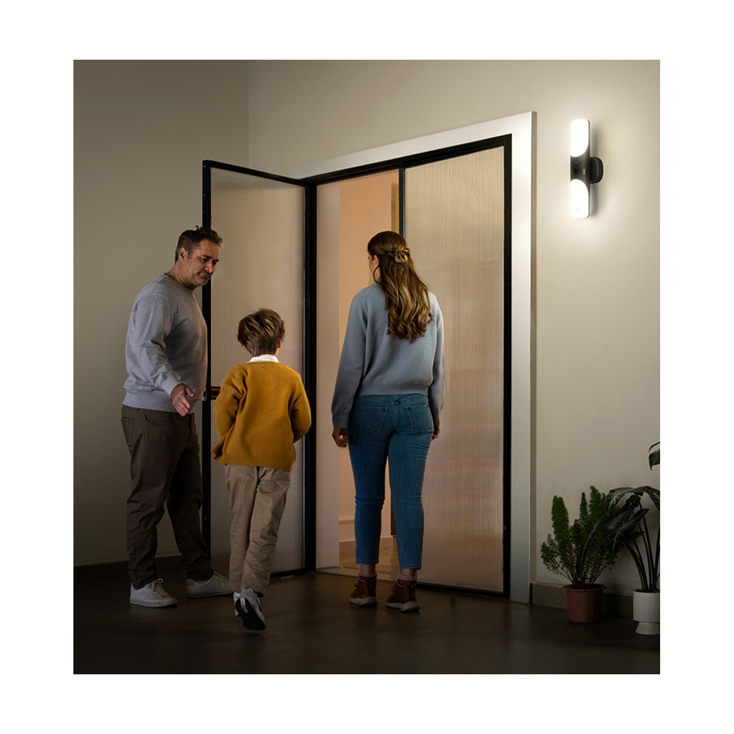 Famille entrant dans une maison, avec un homme, un garçon et une femme, près d'une porte.