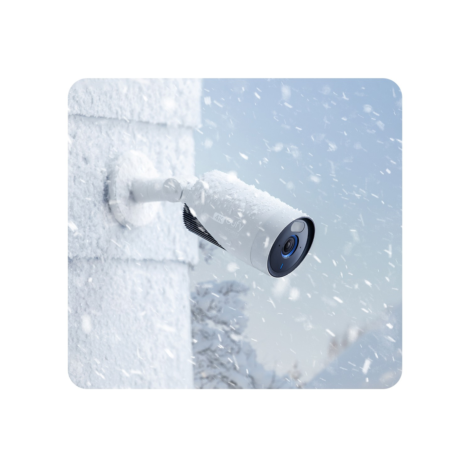 Une caméra de sécurité blanche montée sur un mur blanc, dans un environnement enneigé avec de la neige qui tombe.
