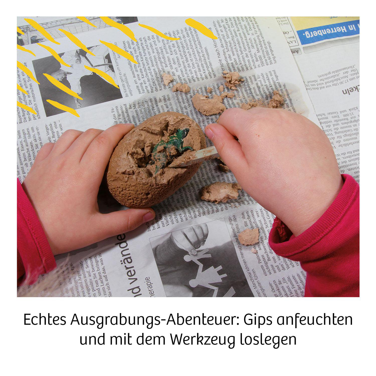 Ein Kind gräbt mit Werkzeugen auf Zeitungspapier ein Gipsobjekt aus.