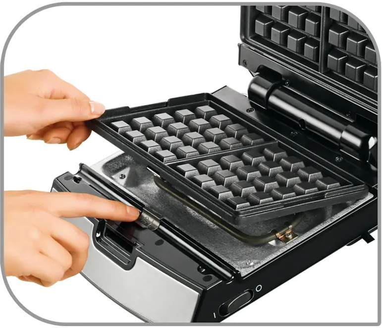 Mani che inseriscono una piastra per waffle nell'apparecchio, aperto, nero e argento.