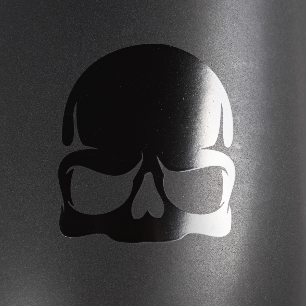 Nahaufnahme einer schwarzen Totenkopf-Silhouette auf dunklem, strukturiertem Hintergrund.