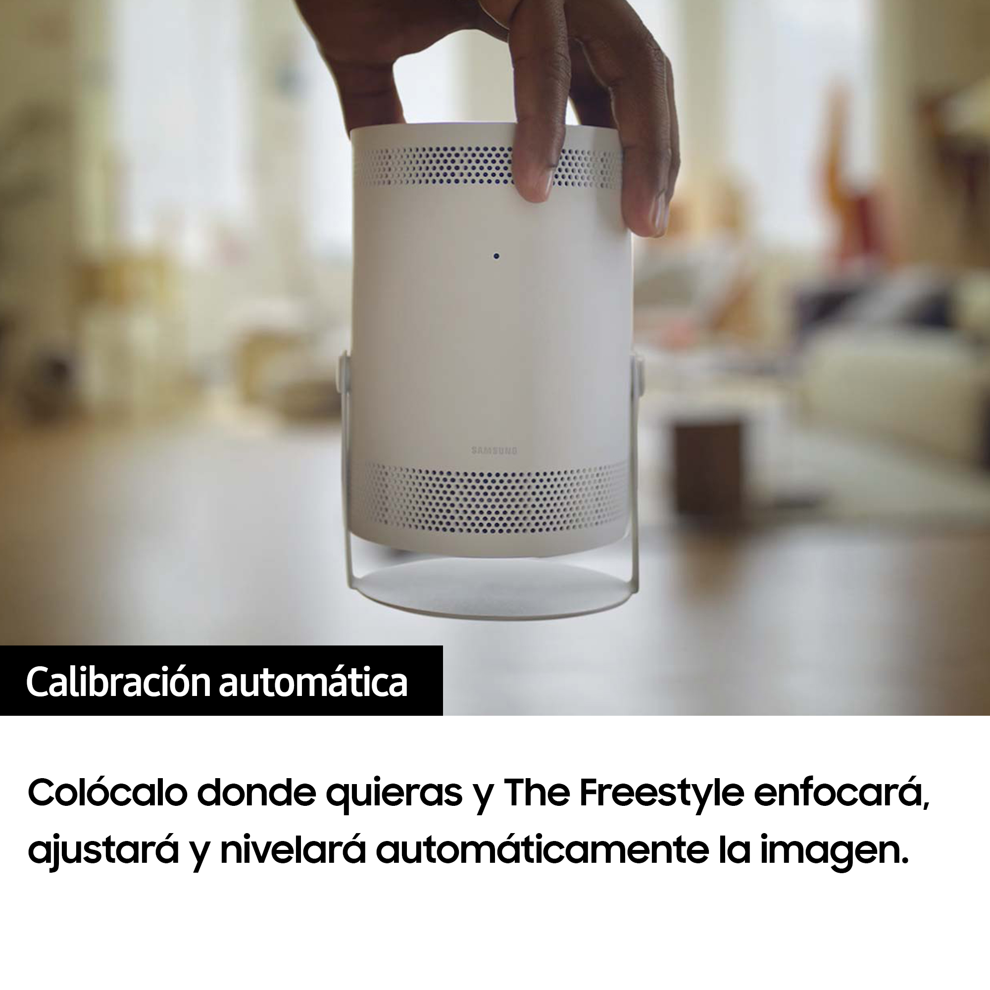 Una mano sostiene un proyector cilíndrico blanco. El fondo es una sala de estar borrosa.