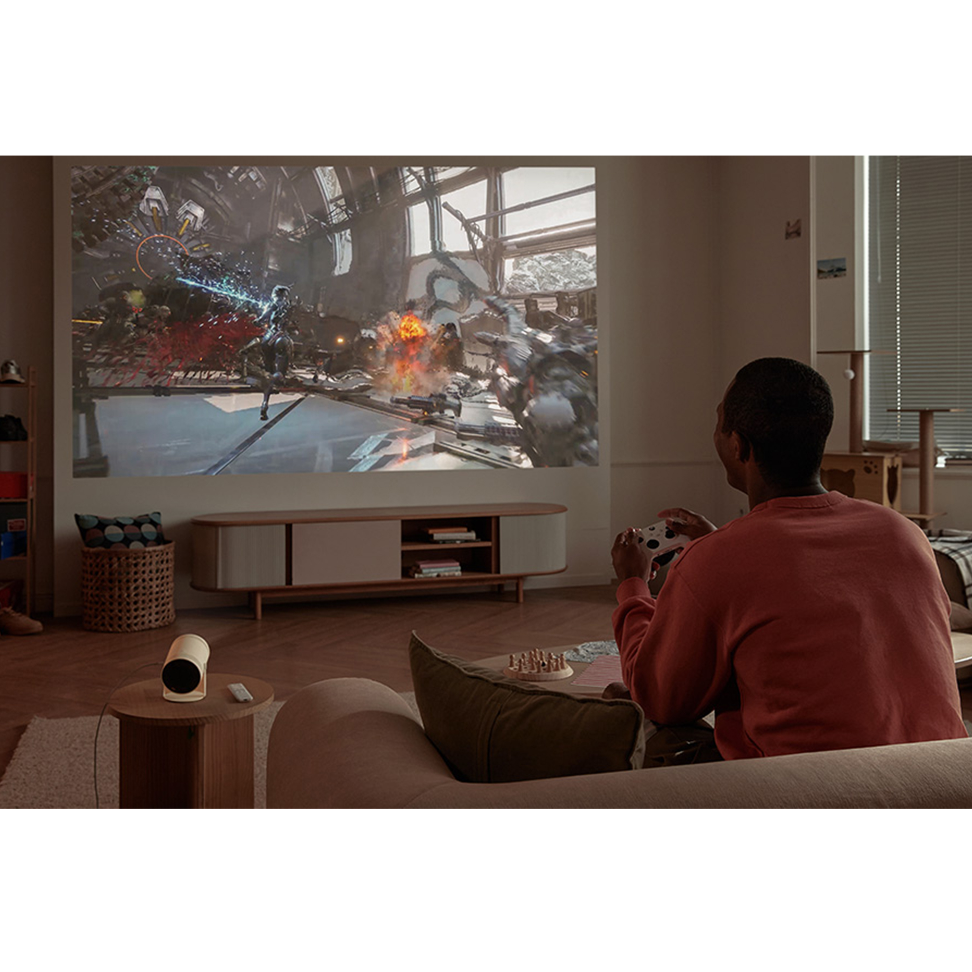 Una persona jugando un videojuego en una pantalla grande usando un proyector. Un proyector y una mesa pequeña.